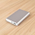 A silver power bank with a USB port on a wooden surface, featuring a sleek, minimal design and a logo.