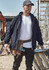 A man wearing a black unisex lightweight packable rain jacket, standing at a construction site with tools and equipment around.