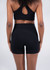 Black high-rise legging shorts featured on a model from the back, paired with a matching sports bra.