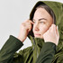 A woman adjusts the hood of a green jacket. The jacket features a logo and has a sleek design.