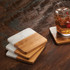 A set of four coasters featuring a marble and bamboo design in white and natural wood tones, set on a wooden surface.