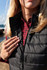 A black puffer vest is partially zipped, worn over a red and black checked shirt. The vest has a logo on it.