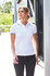 A white ladies polo shirt with navy blue collar and sleeve trims, featuring a logo. Model is walking outdoors.