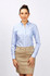 A woman in a light blue button-up long sleeve shirt paired with a beige skirt, standing against a plain background.