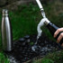 A drink bottle featuring a sleek black design, alongside a stainless steel bottle and two smaller containers on grass.