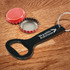 A drink bottle opener key ring in black, with a red bottle cap beside it and a metallic cap inside.