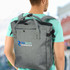 A grey tote backpack with adjustable straps and a logo on the front, worn on a person's back.