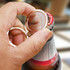 A drink bottle opener key ring in gold and silver, being used to open a bottle cap. It features a logo.