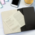 A Moleskine Cahier Journal in black with lined pages, accompanied by a smartphone and a glass of drink.