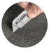 A hand holding a utility knife against a textured grey surface. The knife features a retractable blade.