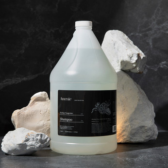 Amenie Sicilian Tangerine Shampoo gallon bottle styled with towel, soap, and bath sponge for a clean spa vibe