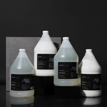 Amenie Sicilian Tangerine Conditioner, Shampoo, and Body Wash gallon bottles on a dark stone background