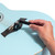 Tiger guitar string winder removing bridge pins from a light blue acoustic guitar bridge during string replacement.