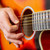 Close-up of an acoustic guitar being played with a pick, showing bronze strings, sound hole and fretboard.