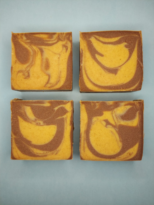 Image shows a side view of 4 bars of soap. Soap has brown and yellow swirls.