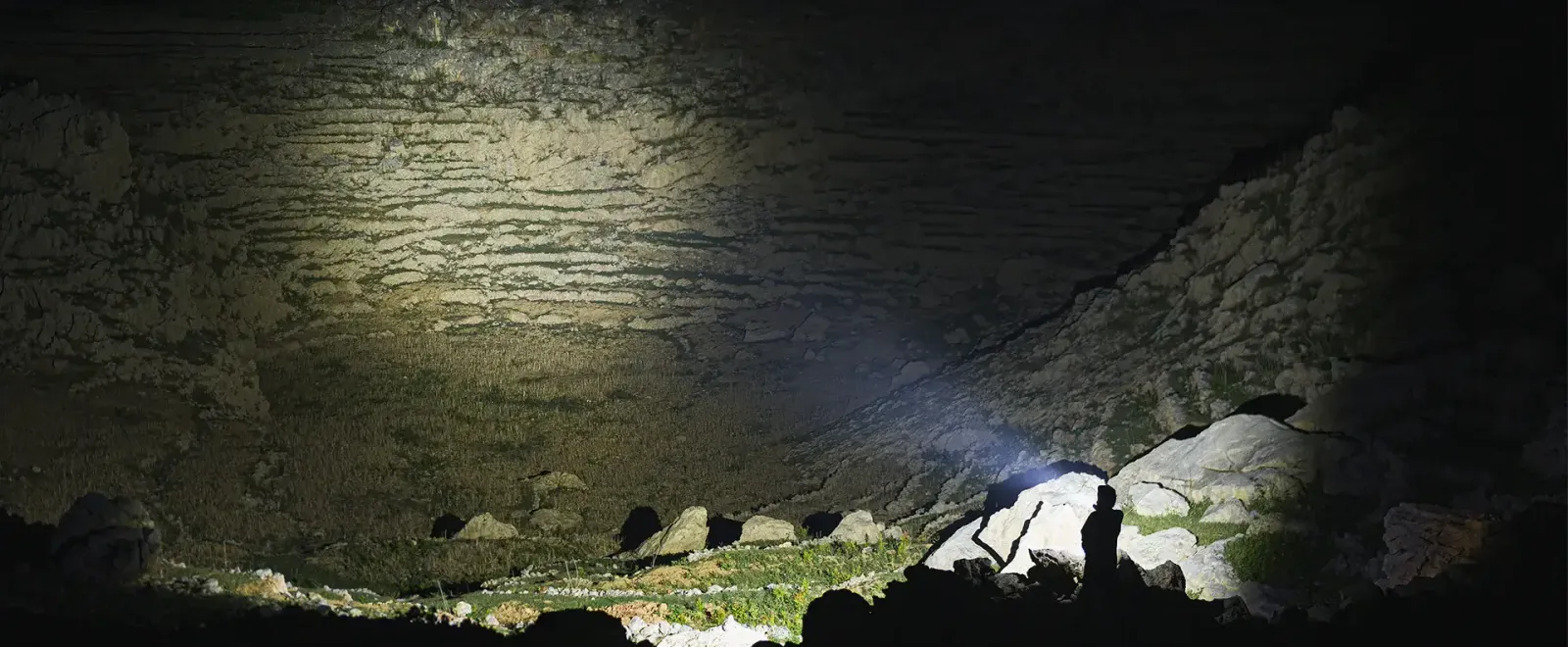 Powerful beam from the Nitecore X1 Pro flashlight illuminating a dark, rocky cave or outdoor landscape.