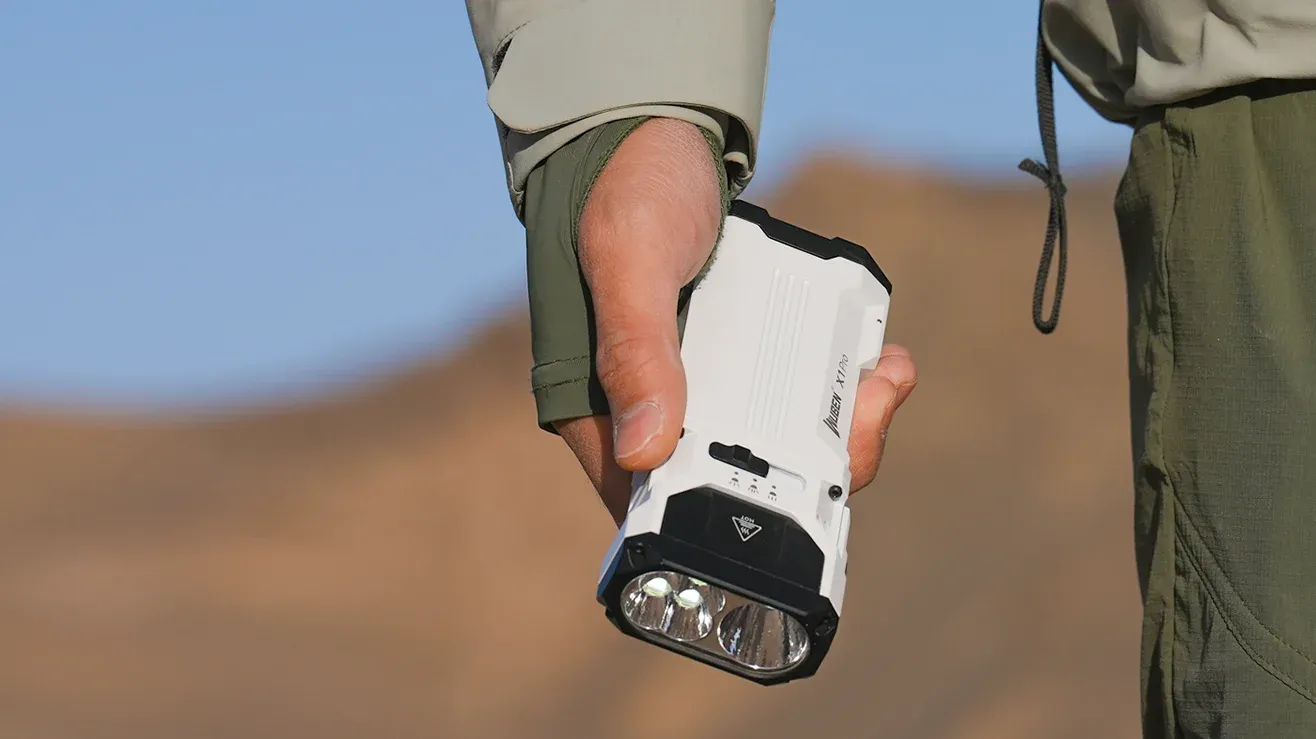 A hand holding the white NUBEN X1Pro flashlight outdoors against a blurred desert-like background.