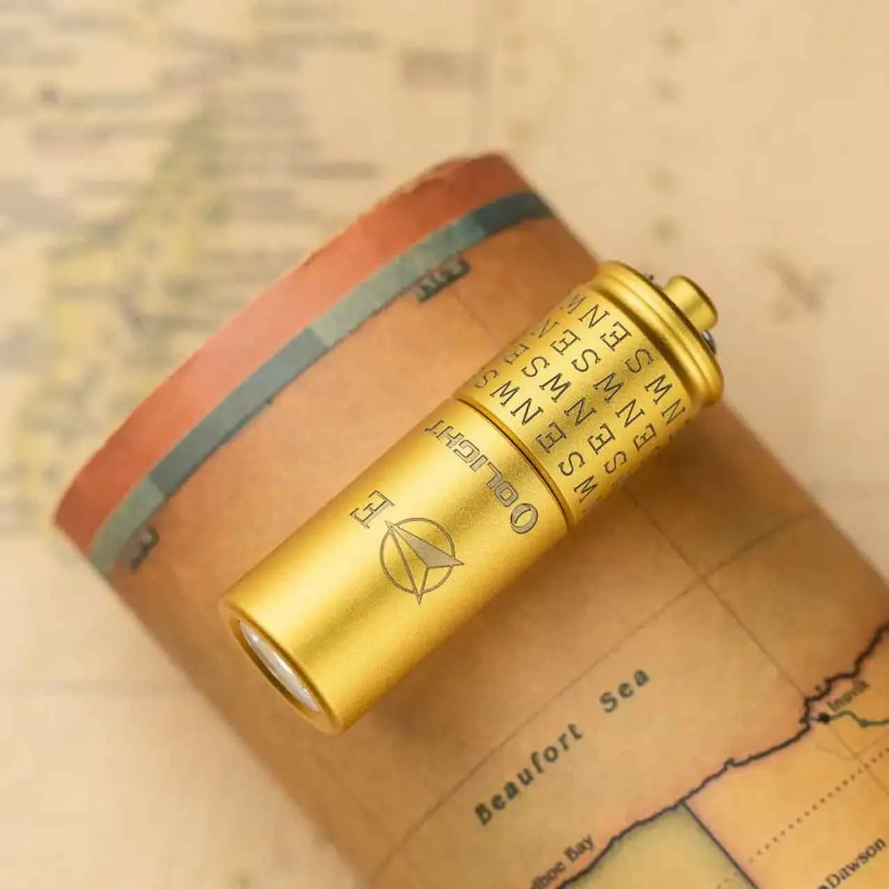 Close-up of the Olight i1R 2 Pro Cardinal Directions Limited Edition 180 Lumen Keychain Light (East) in gold on a map.