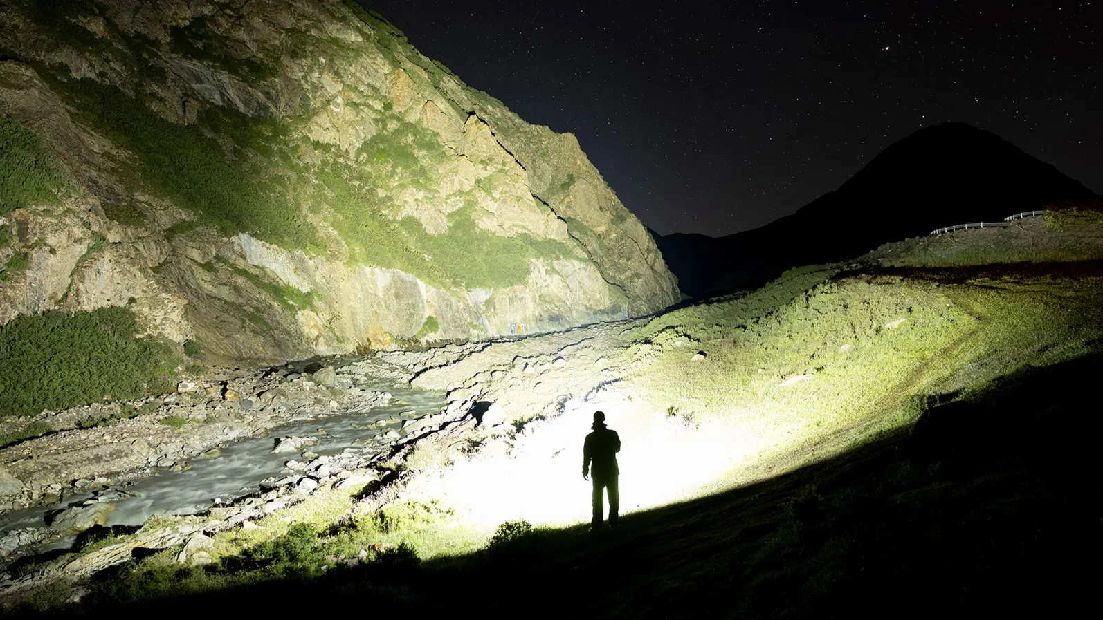 Olight Marauder 3 25000 Lumen Spot and Flood Rechargeable Torch illuminating a person in a dark mountain landscape.