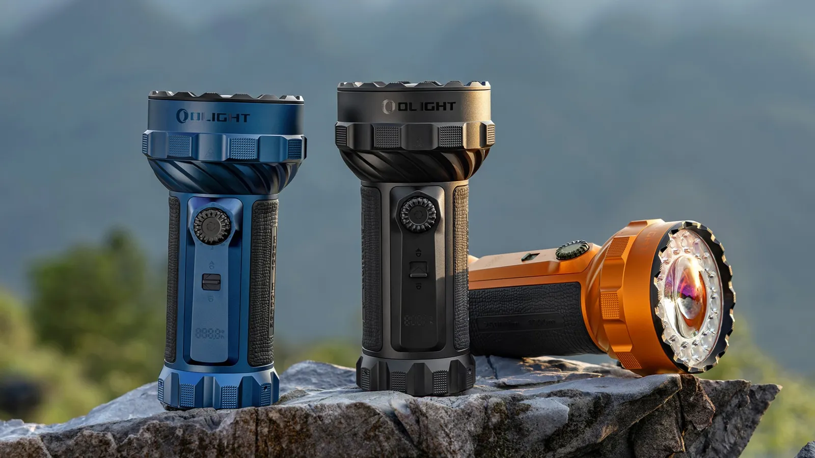Three Olight Marauder 3 25000 Lumen Spot and Flood Rechargeable Torch units in blue, black, and orange.