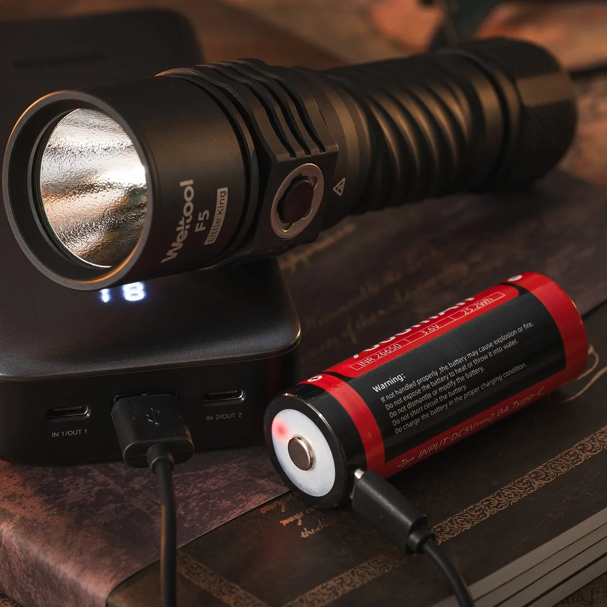 Weltool F5 flashlight next to a power bank, with its removable INR-26650 battery charging via USB-C cable.