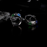 Pair of silver EDC rings featuring vibrant green and blue cut stones on a dark, reflective surface.