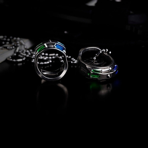 Pair of silver EDC rings featuring vibrant green and blue cut stones on a dark, reflective surface.