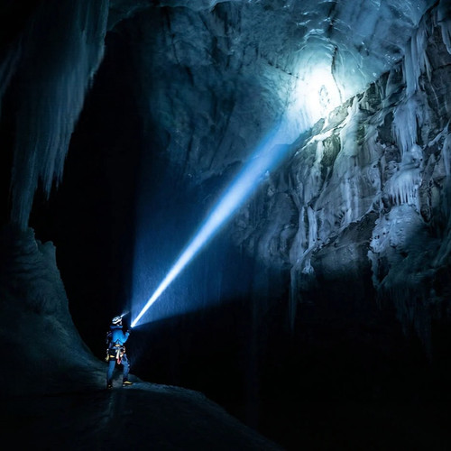 Person illuminating a vast ice cave with the powerful beam of the Acebeam L16 2.0 - 670m Long-Range Tactical Torch.