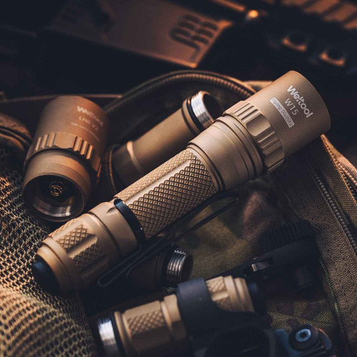 Assembled tan Weltool W15 tactical flashlight with clip, alongside components and gear on a tactical bag.
