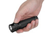 Hand holding the black Olight Baton 4 Pro flashlight, demonstrating its compact size.