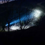 Person using Weltool flashlight at night, powerful beam illuminates trees and hillside.