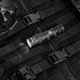 Weltool LH8 W35 tactical flashlight, black, illuminated and lying on black tactical gear with a helmet.