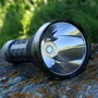 Close-up of the Skilhunt EC500 head, showing its powerful LED emitter and reflective optics on a mossy rock outdoors.