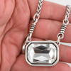 Large, clear, rectangular crystal and silver-plated chain necklace in my hand. 