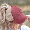 Woman wearing a distressed burgundy ponytail baseball hat featuring a pre-curved bill, tan mesh panels and a high ponytail.