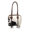 Loyal West Suave black and white hair-on cowhide leather shoulder bag featuring braided brown leather handles, decorative edging, and two vertical zippered pockets.