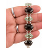 Close-up of faceted smoky quartz and pale green amethyst gemstones connected by decorative sterling silver links in my hand.