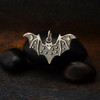 Small sterling silver bat charm pendant shown on rocks.  