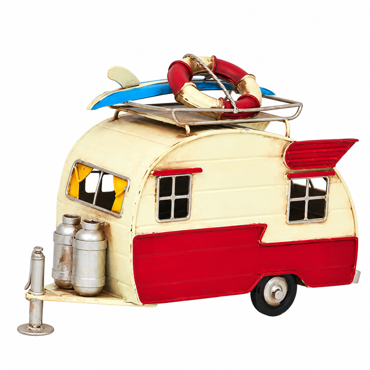 Vintage red and cream metal camper trailer decoration featuring a blue and white surfboard, red and cream life preserver, metal roof rack, miniature propane tanks, detailed windows with yellow curtains, and a distressed retro finish. This decorative travel trailer measures 7.1" long x 4.9" high and is perfect for coastal, beach, and camping-themed décor.