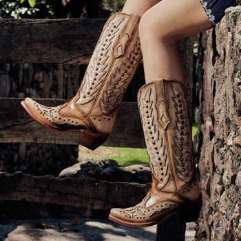 Studded and embroidered overlay wing snip toe sand Corral boot on a model.  