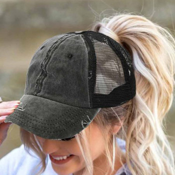 Woman wearing a washed charcoal gray distressed baseball cap with black mesh back and high ponytail opening.