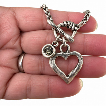 Close-up of a silver-plated open-heart toggle bracelet showing the faceted gray crystal stone, textured heart charm, and antiqued silver finish.