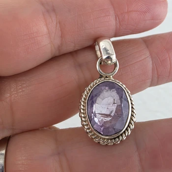 Close-up of oval amethyst sterling silver pendant held in hand showing the natural purple gemstone, faceted surface, polished silver bail and twisted rope border.