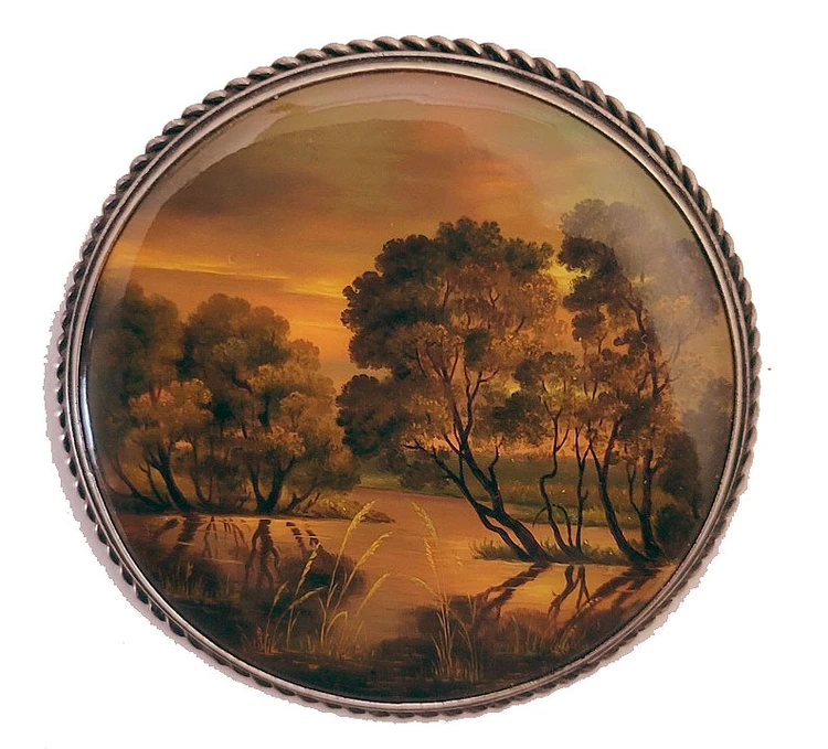 Autumn Sunset (Осенний закат). The painting focuses on the beauty of a glowing setting sun in an open glade in the forest. Delicate miniature oil painting on papier-mache. The piece simply shimmers as the shades of orange and gold play against the dark trees. Fedoskino, circa late 1980s. Materials used are oil paints, lacquer, and metallic powders. Set in aa melchior bezel with a pinback.