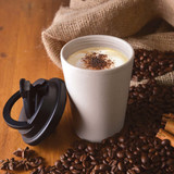 A reusable coffee cup in a light beige color with a black handle lid, surrounded by coffee beans and spices.