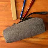 A gray felt utility case with a zipper, accompanied by pens and a highlighter placed on a wooden surface.
