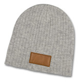 A grey cable knit beanie with a leather patch. The beanie has a soft, textured appearance.