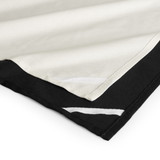 A tea towel featuring a black bottom edge and cream top, with decorative white stitching along the seams.