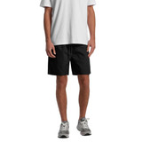 A pair of black sports shorts with an elastic waistband, featured on a model wearing a white T-shirt and grey shoes.