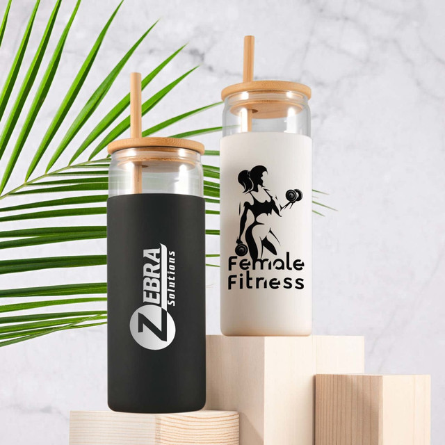 A set of two glass tumblers with bamboo lids, one black and one white, featuring logos and designs.